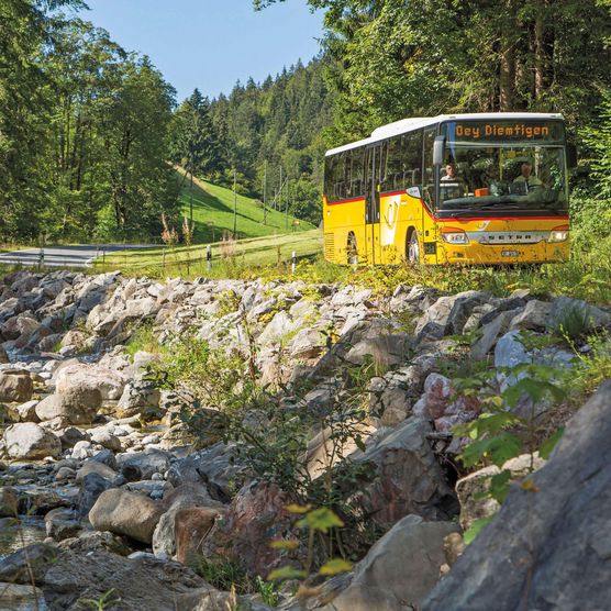 Foto Gelbes Postauto auf der Talstrasse nebem dem Bach - zum Foto