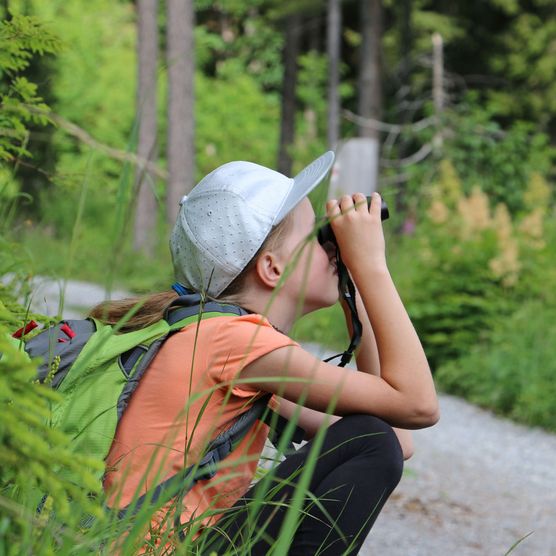 Foto Mädchen sitzt am Wegrand blickt durch ein Fernglas - zum Foto