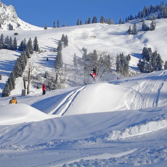 Foto Snowboarder springt über eine Geländekuppe - zum Foto