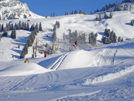 Foto Snowboarder springt über eine Geländekuppe - zum Foto