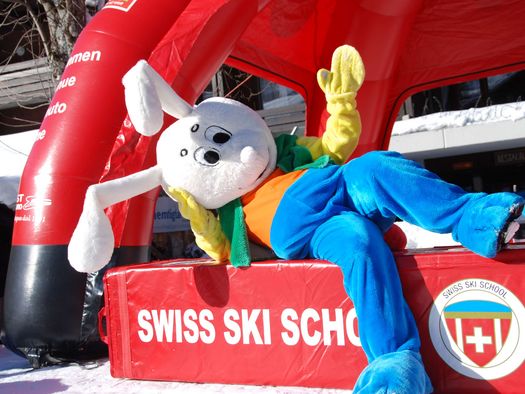 Foto Das Maskottchen Snowli sitzt auf einem Swiss Ski School-Element - zum Foto
