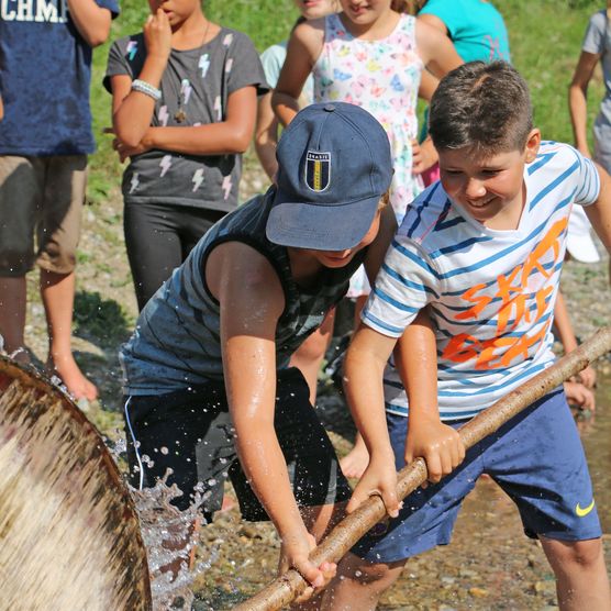 Foto Kinder versuchen mit einem Stecken ein Wasserrad zum Halten zu bringen - zum Foto